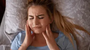 Mulher deitada na cama com dor na mandíbula ao acordar, sintoma comum do bruxismo do sono